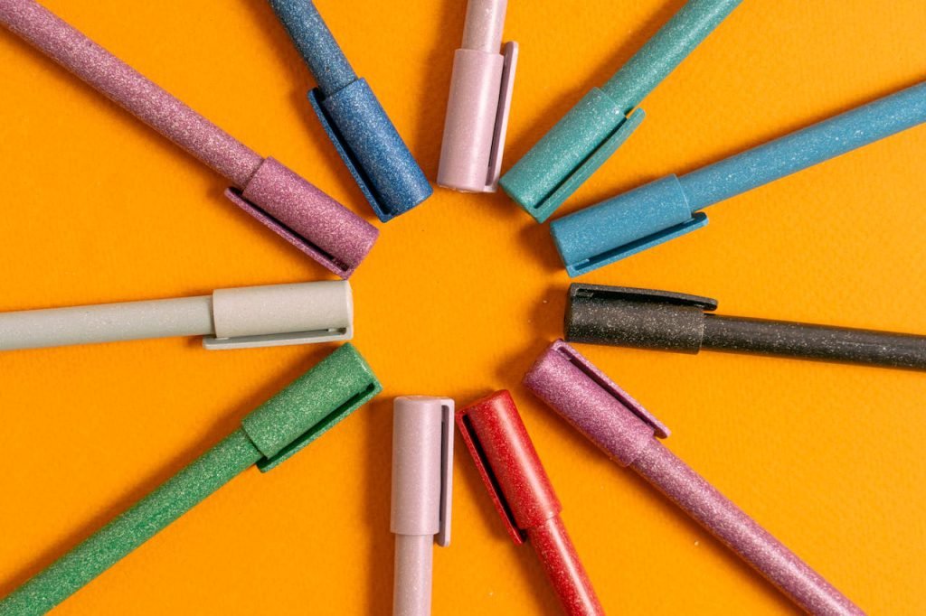 A creative arrangement of glittery pens in a circular pattern on an orange background.