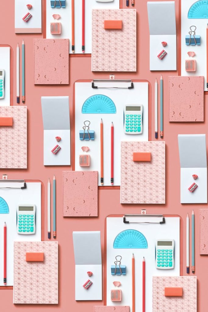 Colorful assortment of stationery items arranged on a pink background in a flat lay style.