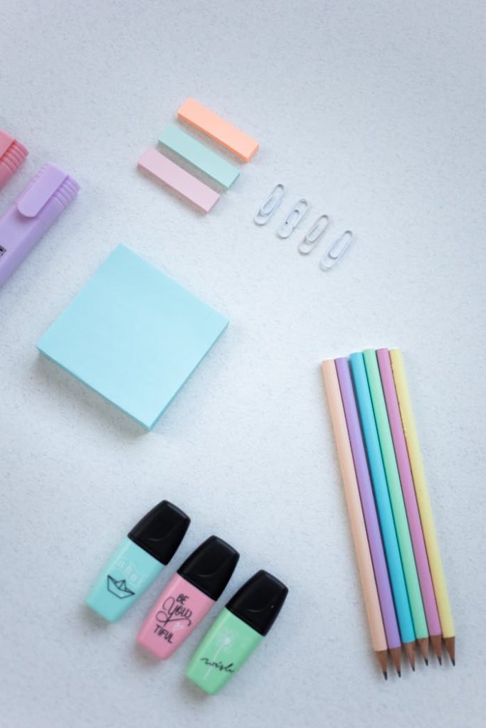 Flat lay of pastel stationery items including pencils, paper clips, and sticky notes on white surface.