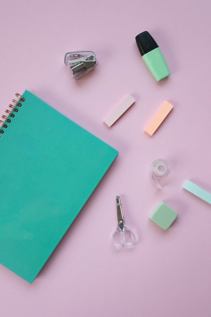 A collection of colorful stationery items arranged on a pastel pink background.