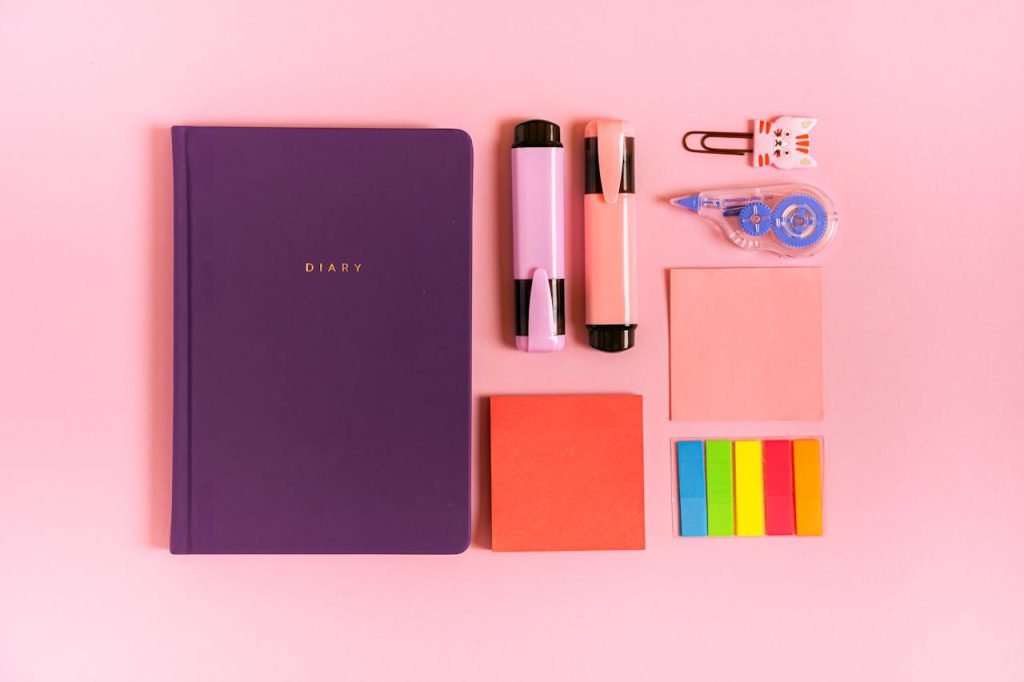 A vibrant flat lay of diary and stationery items on a pink background, perfect for organization.