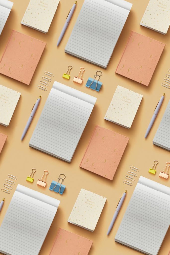 Top view of various stationery items including notepads, pens, and clips arranged on a warm background.